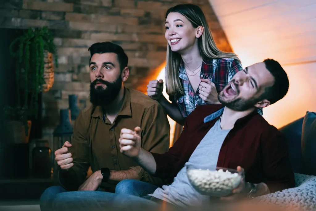 Tres amigos emocionados viendo un partido de fútbol en el sofá de casa con una suscripción IPTV en España